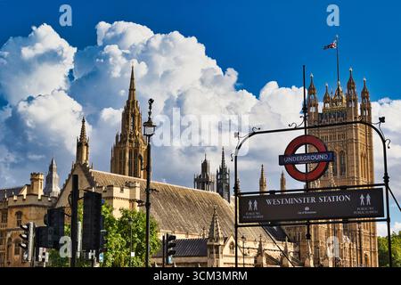 L'iconica stazione di Westminster di Londra, con le Houses of Parliament e Union Jack contro un suggestivo cielo blu con soffici nuvole bianche. Foto Stock