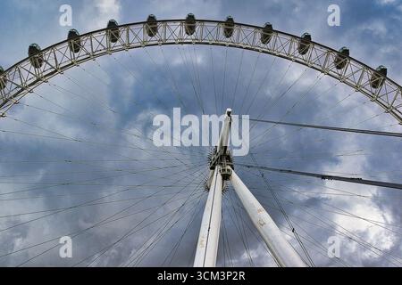 Un'immagine estremamente bassa di una ruota panoramica contro un cielo spettacolare e nuvoloso, che mostra la sua struttura intricata e le gondole. Foto Stock