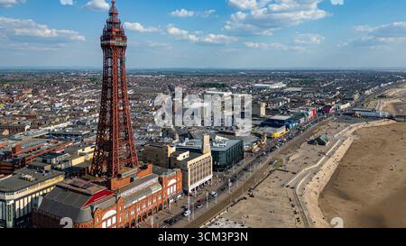 Veduta aerea di una cittadina di mare con un'importante torre di ferro rossa, un'ampia passeggiata, una spiaggia e edifici densamente affollati a Blackpool, Regno Unito. Foto Stock