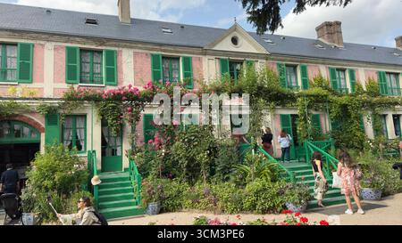 Una casa rosa con persiane verdi, ricoperta di rose da arrampicata, con persone che camminano su scale verdi e nel giardino. Foto Stock