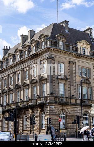 Una vista d'angolo di un grande edificio in pietra ornato a più piani, finestre dormitori e un tetto di mansarda, sotto un cielo blu a Newcastle upon Tyne, U Foto Stock