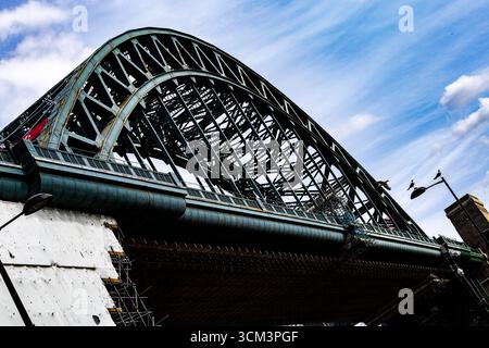 Una vista ad angolo basso di un ponte ad arco in acciaio con una complessa struttura a reticolo contro un cielo blu luminoso con nuvole di neve a Newcastle upon Tyne, Regno Unito. Foto Stock