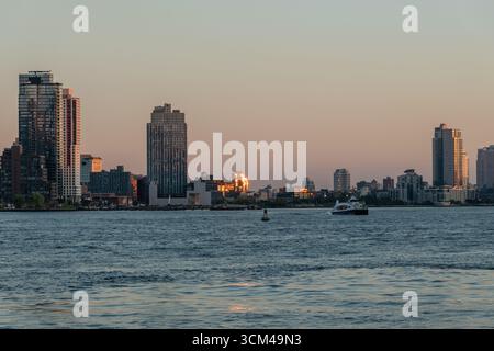 Il sole si riflette nelle finestre dell'edificio al tramonto a Brooklyn lungo la riva dell'East River, vista dall'altra parte del fiume a Manhattan, New York City Foto Stock
