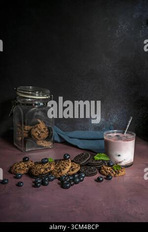 Immagine di una deliziosa colazione o di uno spuntino con biscotti di pasta frolla, un frullato denso di mirtilli e banane in un vaso di vetro e una manciata di frutti di bosco freschi Foto Stock