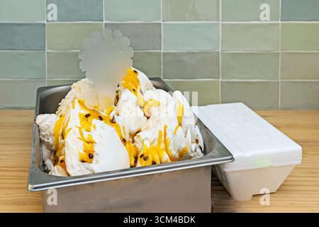 Vasca gelato al mango con pezzi di frutta tropicale, salsa di frutta della passione e cocco grattugiato, evocando sapori esotici e di spiaggia Foto Stock