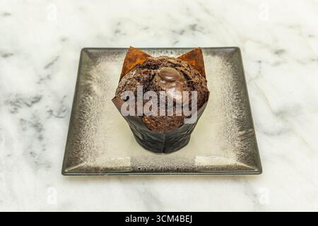 muffin al cioccolato e ai lamponi con vortici rosa, preparati contro la croccante porcellana bianca con un delicato bordo argentato. Foto Stock