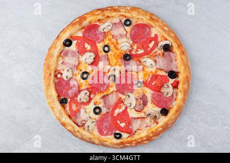 Pizza con pancetta, peperoni, funghi, fette di pomodoro, olive nere e formaggio fuso su sfondo Stone Foto Stock