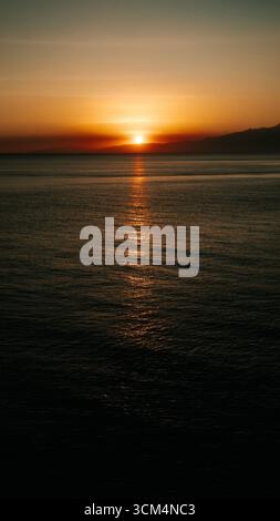 Splendido tramonto che crea una vista estetica in una combinazione di colori rosso, giallo, arancione e motivi che si affacciano sull'oceano, tranquillo e tranquillo Foto Stock