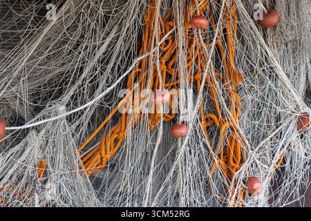 Un'immagine dettagliata delle reti da pesca intrecciate con corde arancioni e galleggianti galleggianti, raffiguranti gli strumenti utilizzati nelle pratiche di pesca tradizionali e la i Foto Stock