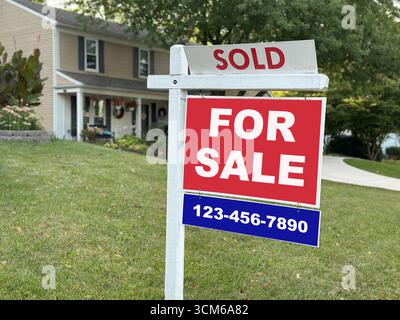 Una casa residenziale con un cartello in vendita contrassegnato come venduto nel cortile anteriore. Il segno rosso e bianco con un numero di telefono rappresenta le transazioni immobiliari, l'acquisto di abitazioni e la vendita di immobili. Foto Stock