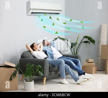 Coppia felice che riposa sul divano a casa. L'aria condizionata mantiene una temperatura confortevole in camera Foto Stock