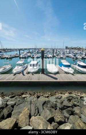 Porticciolo di Mazagón, con barche di varie dimensioni ormeggiate in una giornata di sole con acque calme e frangiflutti circostanti. Foto Stock