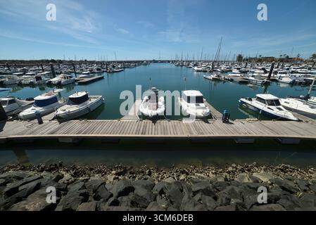 Porticciolo di Mazagón, con barche di varie dimensioni ormeggiate in una giornata di sole con acque calme e frangiflutti circostanti. Foto Stock