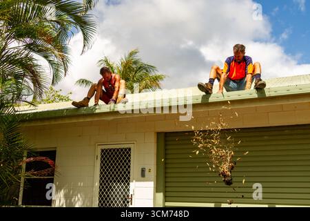 un uomo al di sopra della porta uno al di sopra del tetto della porta del garage lascia le mani che cadono gettando poche foglie sopra le grondaie che puliscono le grondaie del tetto Foto Stock