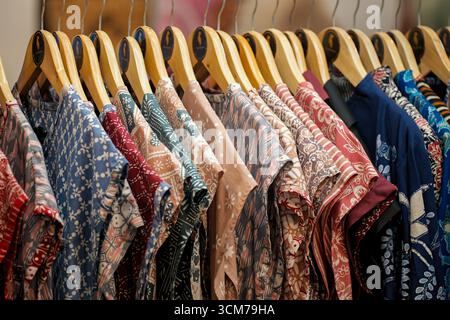 Una fila di camicie colorate appese su appendiabiti in legno in un negozio al dettaglio Foto Stock