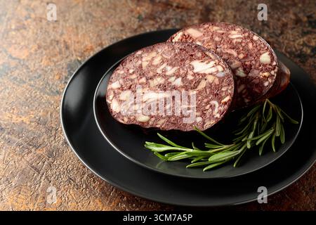 Salsiccia di sangue con frattaglie di carne accompagnata da rosmarino su un piatto nero. Foto Stock