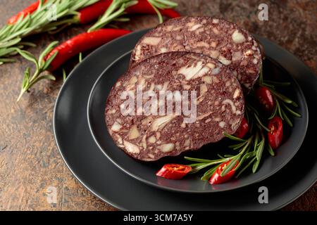 Salsiccia di sangue con frattaglie di carne accompagnata da rosmarino e pepe rosso su un piatto nero. Foto Stock