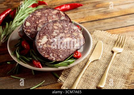 Salsiccia di sangue con frattaglie di carne accompagnate da rosmarino e pepe rosso su un tavolo di legno. Foto Stock