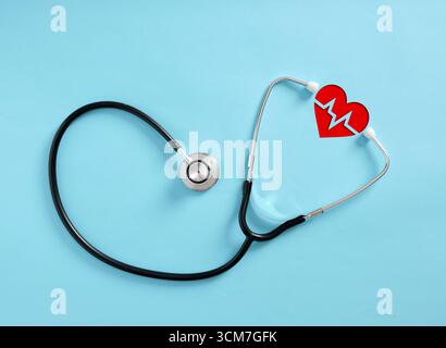 Stetoscopio che incornicia un cuore rosso con linea ekg appoggiato su uno sfondo blu, che rappresenta la salute cardiovascolare e l'assistenza medica Foto Stock