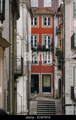 Stretti scalini di pietra che conducono al colorato edificio portoghese nel quartiere storico di Porto. Facciata rossa, architettura, scalinata ripida, Urban Alley Foto Stock