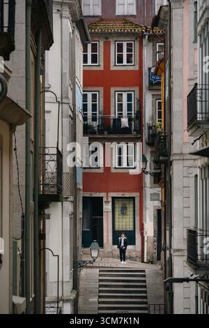 Persona che arrampica i gradini di pietra verso il colorato edificio portoghese nel quartiere storico di Porto. Architettura tradizionale, scalinata ripida, esplorazione urbana Foto Stock