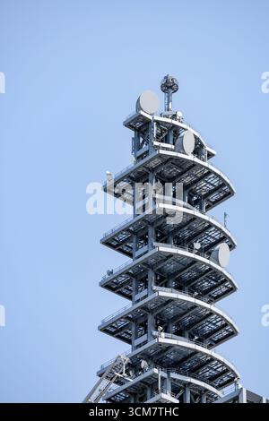 Torre di comunicazione a più livelli con più antenne e antenne satellitari disposte contro il cielo azzurro. Travi metalliche e piattaforme leggermente curve visibili. Foto Stock