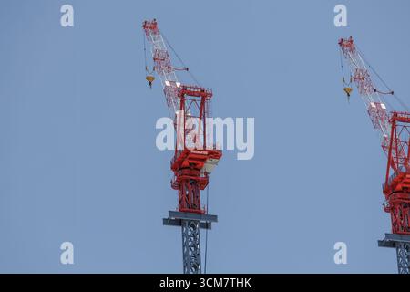 Due torreggianti gru da costruzione rosse-bianche. I bracci si estendono in alto contro il cielo cristallino, simboleggiando lo sviluppo urbano in una costruzione moderna. Foto Stock