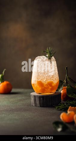 Cocktail rinfrescante con ghiaccio, fette di mandarino e rosmarino sulle montagne russe in legno Foto Stock