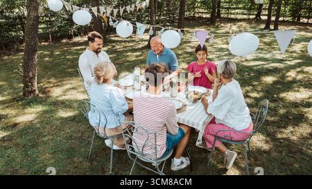 Vista aerea dei nonni, dei genitori e dei bambini che mangiano insieme all'esterno. Foto Stock