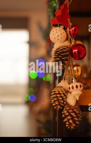Primo piano delle decorazioni natalizie con coni di pino, ornamenti rossi e bianchi e luci soffuse di bokeh. Atmosfera festosa accogliente, caldo sfondo delle vacanze Foto Stock