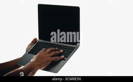 Vista ravvicinata delle mani che gestiscono un notebook con schermo nero vuoto, isolato su uno sfondo bianco minimalista. L'immagine richiama un senso di Foto Stock