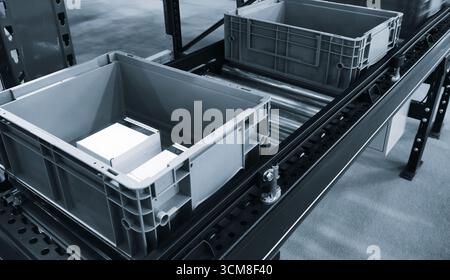 Nastro trasportatore con due contenitori di plastica vuoti. Contenitori grigi posizionati sul nastro trasportatore. Concetto di stoccaggio del magazzino logistico di consegna. Foto Stock