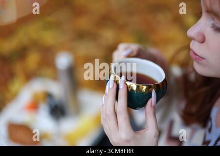 Momenti autunnali accoglienti con una tazza calda di tè in mano, circondati da colorate foglie autunnali. Foto Stock