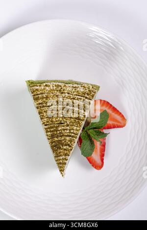 Fetta di cheesecake agli spinaci con fragole e vista dall'alto alla menta su sfondo bianco Foto Stock
