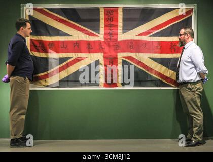 Londra, Regno Unito. 15 settembre 2025. Il curatore Dr Alan Jeffreys e il Conservatore Joshua Seymour con una bandiera dell'unione catturata da un edificio a Singapore dal sergente maggiore Uchiyama, che lo ha iscritto 'Singapore Defess Memorial Uchiyama' 15 febbraio 1942. "Beyond Burma: Forgotten Armies" al Museo Nazionale dell'Esercito segna 80 anni dalla campagna birmana nella seconda guerra mondiale e fa luce sugli eserciti "dimenticati" che vi hanno servito. La mostra si svolge fino al 13 aprile 2026. Crediti: Imageplotter/Alamy Live News Foto Stock