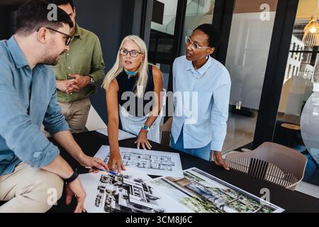 Un gruppo eterogeneo di colleghi partecipa a una discussione sui piani architettonici. La loro collaborazione dimostra il lavoro di squadra, la risoluzione creativa dei problemi, un Foto Stock