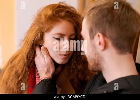 Un uomo e una donna si stanno abbracciando. La donna ha i capelli rossi. Quell'uomo indossa una giacca nera Foto Stock