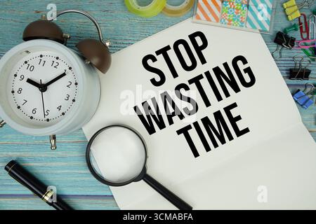 Basta perdere tempo testo scritto su blocco note con sveglia e lente d'ingrandimento piatta su sfondo in legno Foto Stock