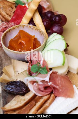 Primo piano di un tagliere di salumi con un assortimento di formaggi, affettati, fette di mele verdi fresche, uva, grissini, cracker, Foto Stock
