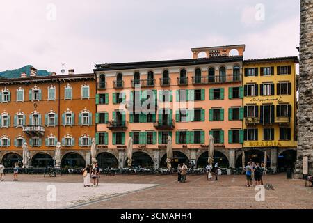 Riva del Garda, Italia - 20 agosto 2025: Una vivace piazza cittadina a Riva del Garda, Italia, caratterizzata da un'architettura storica e da persone che si godono la giornata. Foto Stock