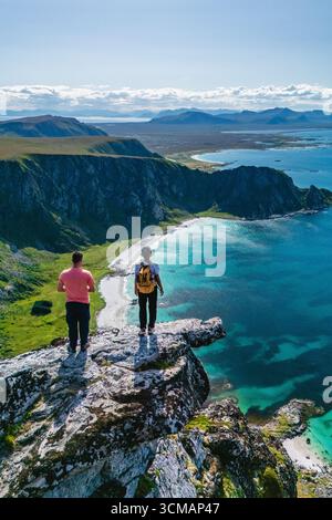 Goditi panorami mozzafiato dalla cima del monte Matind, dove due escursionisti ammirano le splendide spiagge e le acque turchesi di Bleik e Andoya sotto un cielo azzurro, una perfetta avventura all'aria aperta. Foto Stock
