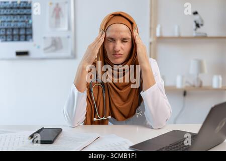 Esausto musulmano arabo donna Dottore ha sottolineato sofferenza mal di testa durante il lavoro utilizzando il computer in ufficio ospedaliero. Medicina e assistenza sanitaria Foto Stock
