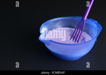 Prodotto cosmetico biondo per la cura dei capelli. Polvere nel recipiente e spatola su sfondo nero, primo piano. Spazio per il testo Foto Stock