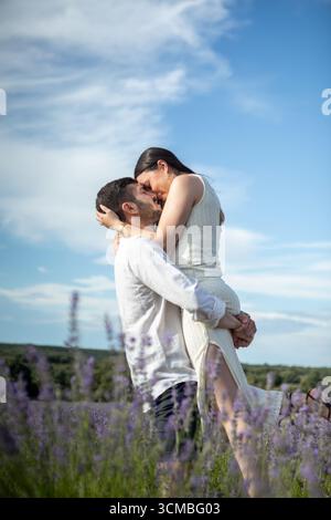Una coppia amorevole condivide un tenero abbraccio in un vivace campo di lavanda sotto un cielo azzurro, catturando un momento di romanticismo e connessione nel cuore Foto Stock