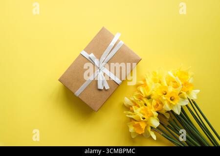 Bouquet di narcisi e una confezione regalo su sfondo colorato, vista dall'alto con spazio per il testo. Fiori primaverili freschi. Foto Stock