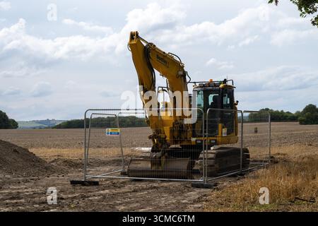 escavatore di ellisse dietro la recinzione di sicurezza nei terreni agricoli, macchinari pesanti per l'edilizia in cantiere sotto il cielo estivo nuvoloso in campagna Foto Stock