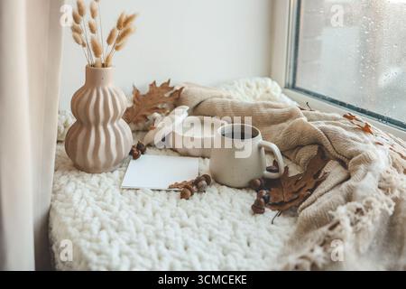 Tazza di tè, candela, plaid e foglie nell'interno della casa autunnale. Foto Stock
