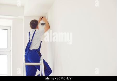 Un tecnico maschile installa telecamere di sorveglianza sulla parete per la sicurezza negli uffici. Foto Stock