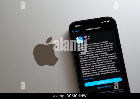Aggiornamento in modalità oscura iOS 26 su iPhone accanto al logo Apple su MacBook, viene visualizzato il prompt Aggiorna ora. Stafford, Regno Unito, 15 settembre 2025 Foto Stock