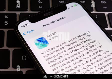 Dettagli dell'aggiornamento di iOS 26 su iPhone con sfondo della tastiera MacBook, testo e icona a fuoco. Stafford, Regno Unito, 15 settembre 2025 Foto Stock